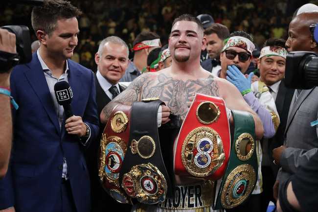 Andy Ruiz holding his belts, surrounded by people, in the ring